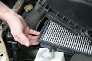 An auto mechanic removing the dirty air filter from an automobile.   Photo taken as work was actually being performed.