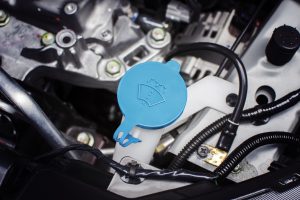 Windshield washer fluid cap with blue color in engine room of car, automotive part concept.