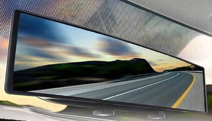 A car rearview mirror displays a view of an empty road, mountains, and blue/pink sky.