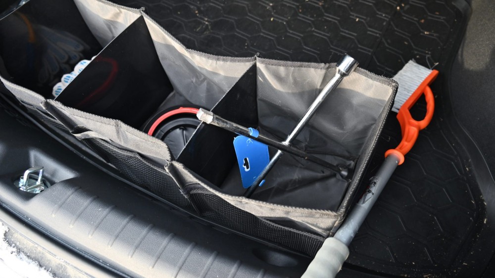 A trunk organizer inside of a trunk with an ice scraper on it.