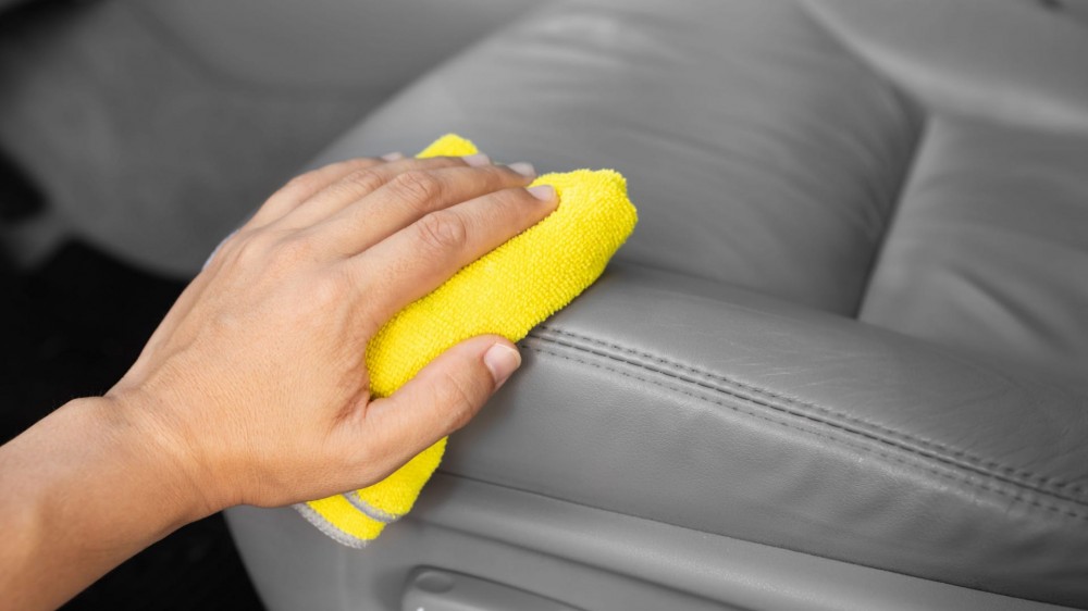 Hand with microfiber cloth applying conditioner to car leather seat interior.