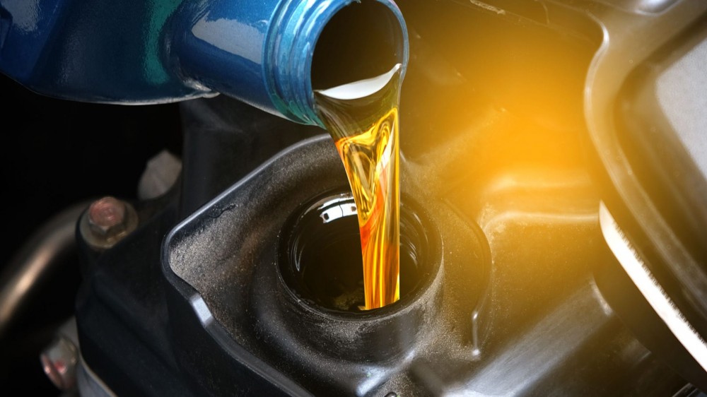 Pouring motor oil into a car engine from a blue bottle.