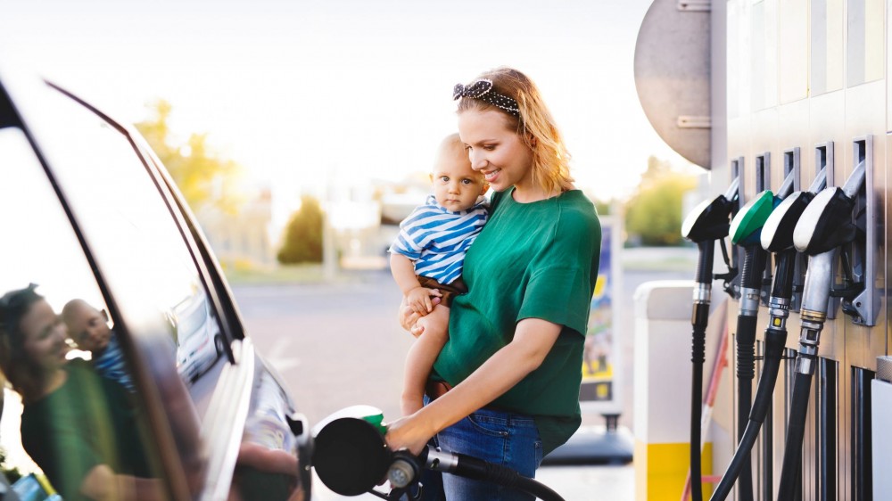 A woman pumps gas while holding a child.