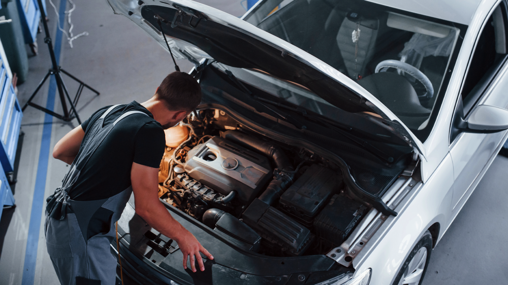 A mechanic looking under the hood of a car.